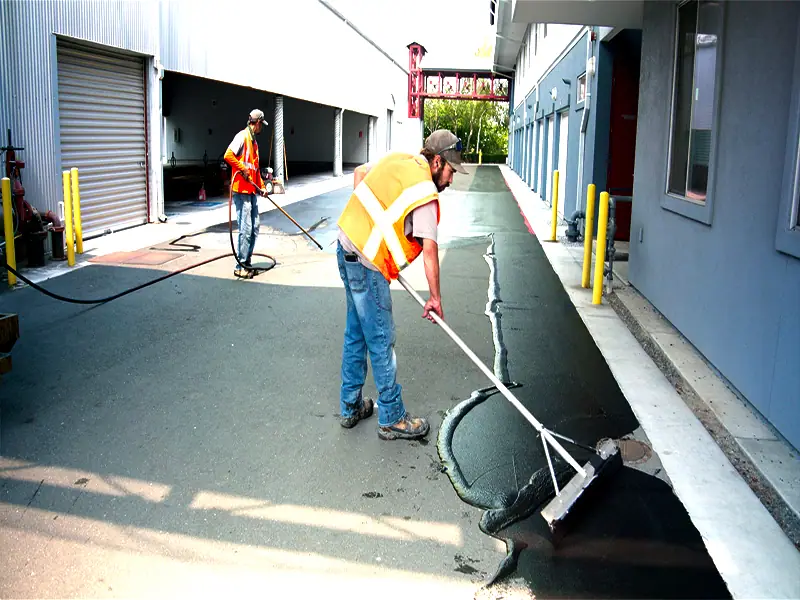 Crew squeegeeing sealcoat along a row of garages