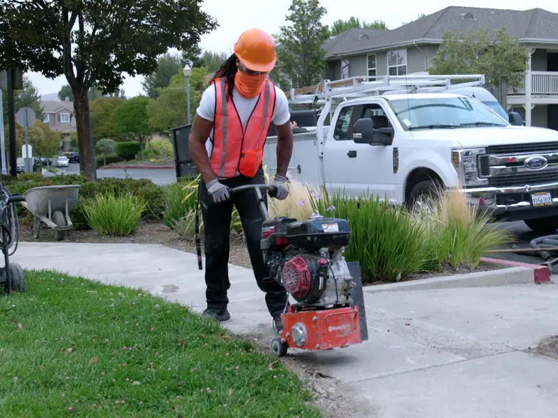 Crew member grinding down a sidewalk trip hazard at an apartment community