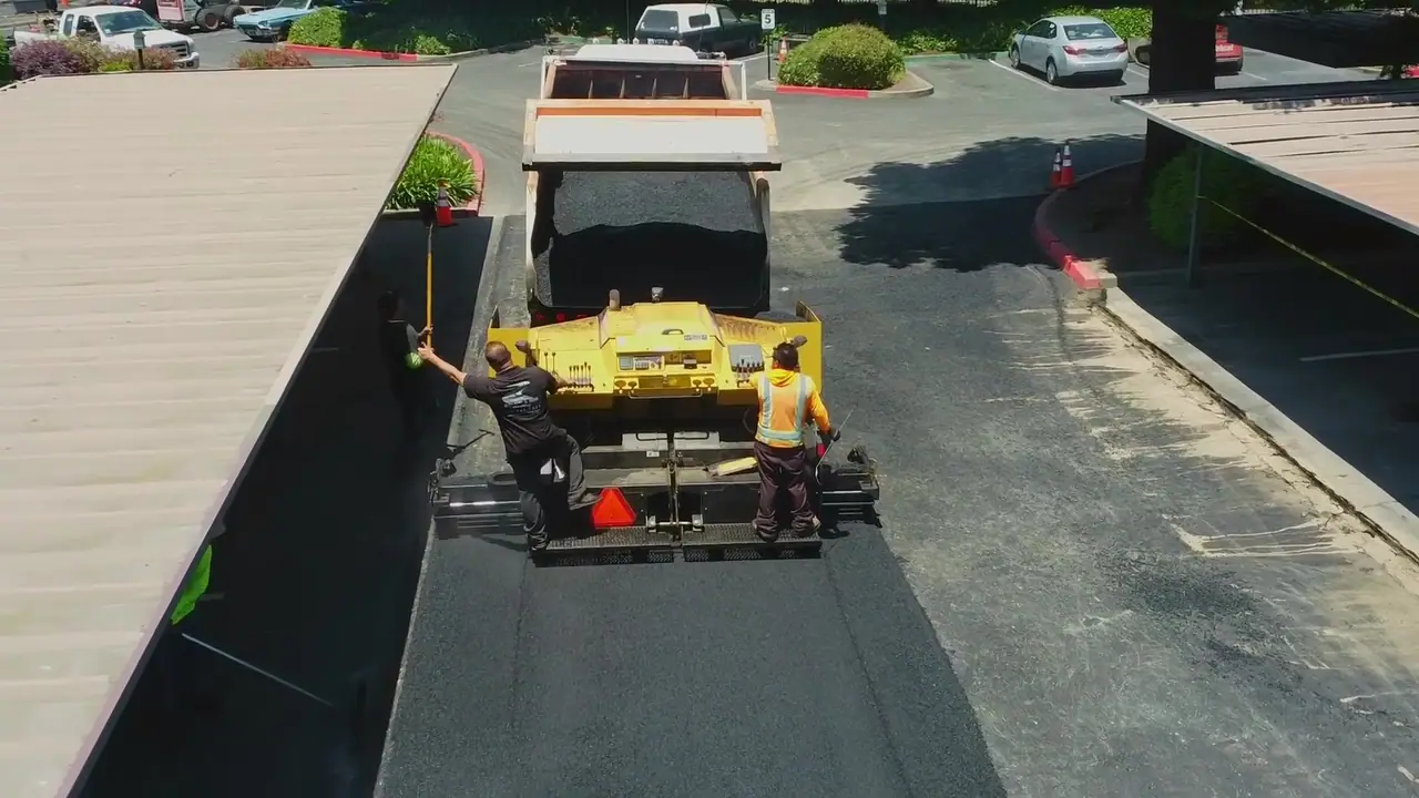 Paver laying new asphalt beside a row of carports